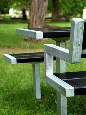 Close up image of a park bench and table, you can see detailing of the steel armrest and the steel frame.